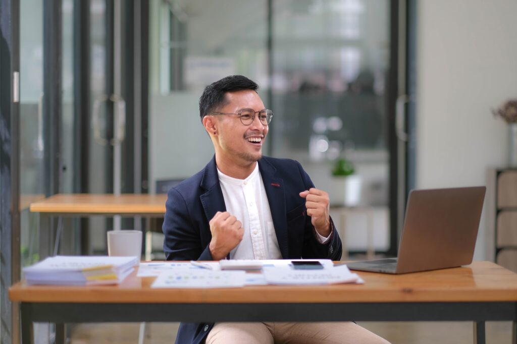 Portrait of an Asian male business owner standing with a computer showing happiness after a