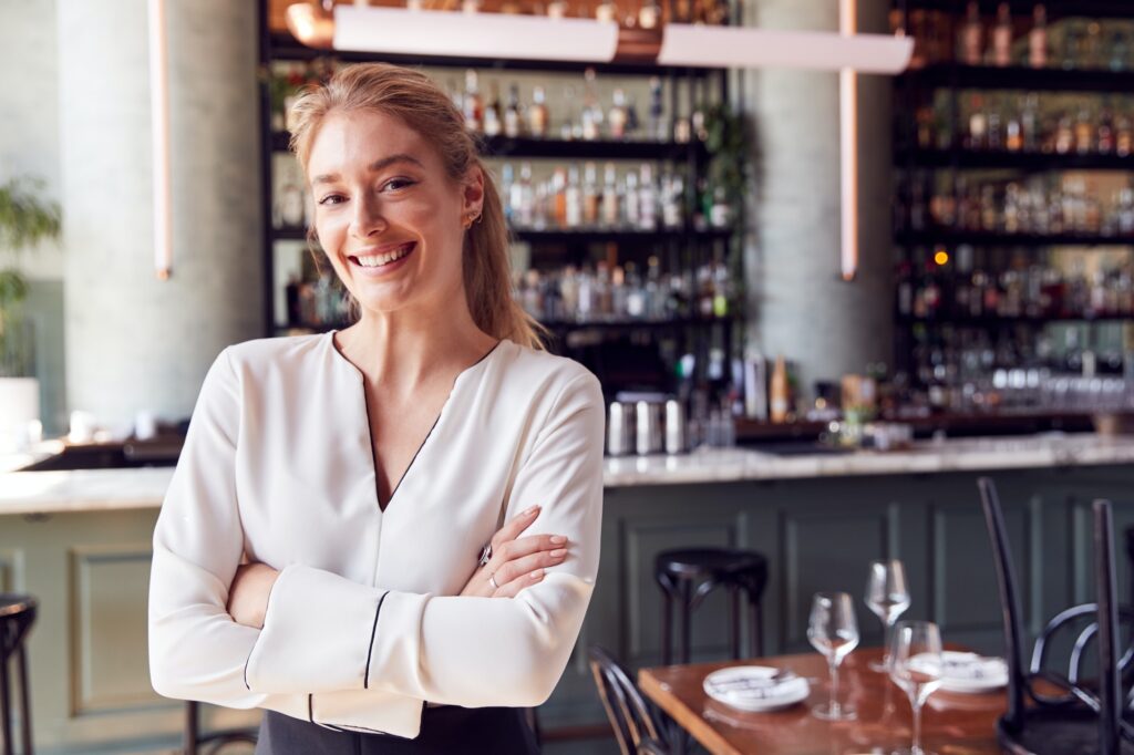 Portrait Of Confident Female Owner Of Restaurant Bar Standing By Counter