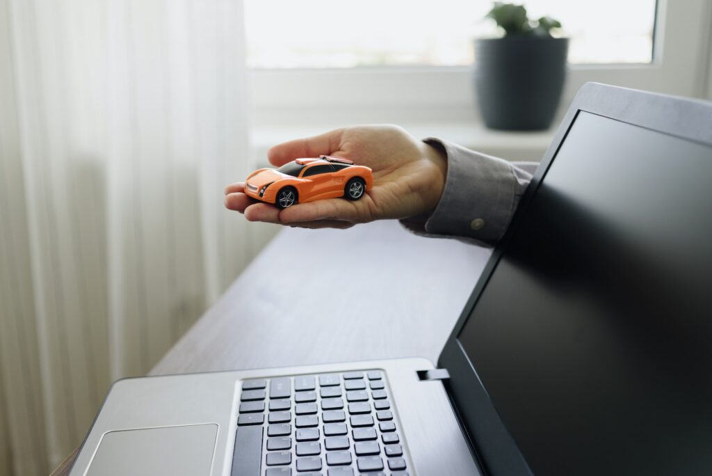 Hand with unrecognized car and laptop. Buying new car