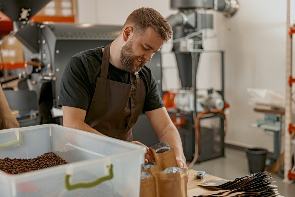 Business owner in uniform packs roasted coffee beans into packages for sale