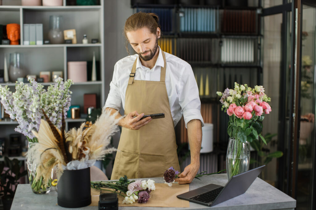 Florists making bouquet of flowers on counter and taking photo on smartphone for social media.