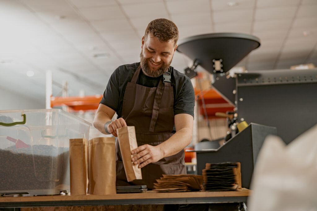 Business owner weighs paper bag with coffee beans on a scale at coffee factory