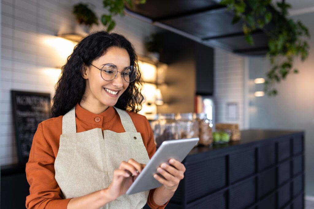 Female barista waitress inside cafe using tablet, latin american restaurant owner smiling using