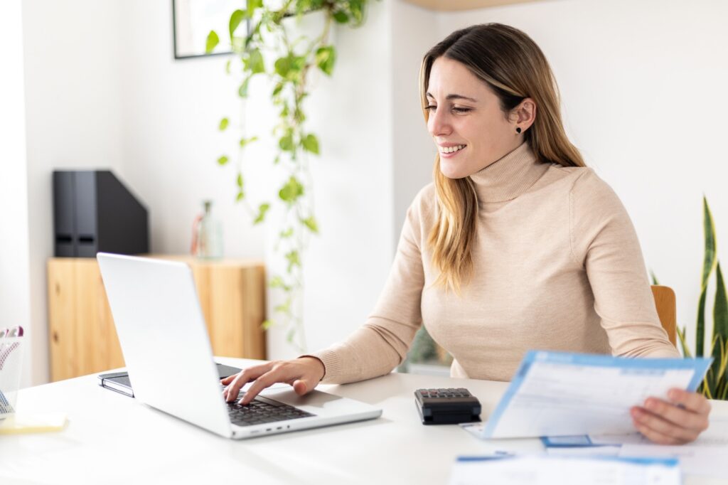 Smiling young woman consulting business invoices sitting on desk