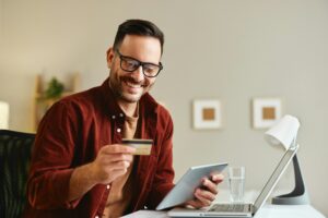 young man holding credit card and tablet at home at table 300x200 - The Best Finance Podcasts to Help Your Small Business