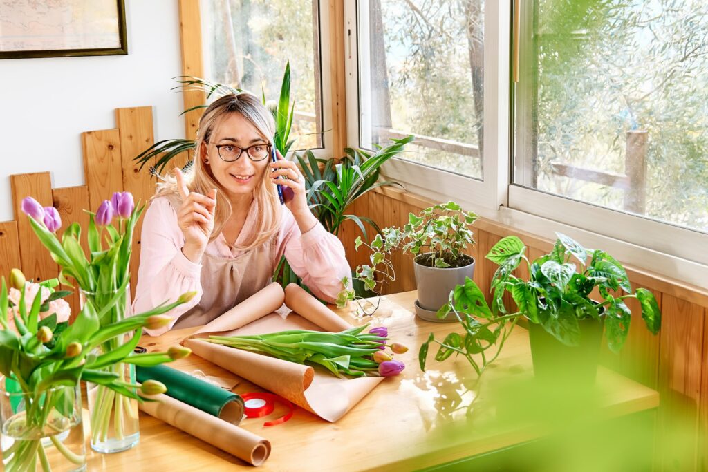 Woman florist in flower shop taking order by mobile phone. Social media for small business.